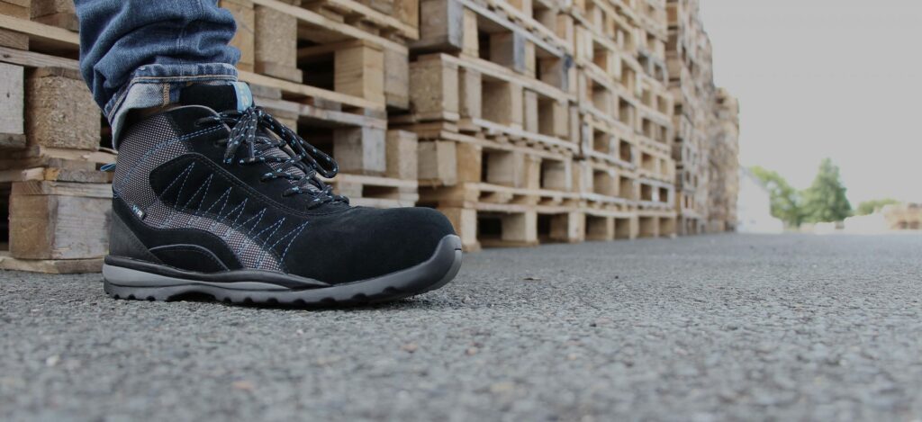 chaussure de sécurité montante noire et grise prise de profil devant des palettes en bois