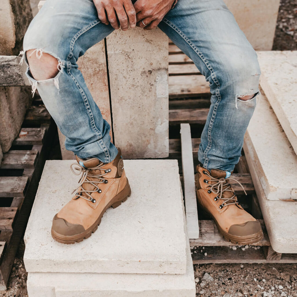 homme assis sur des blocs de pierre habillé avec un jeans et des chaussures de sécurité couleur crème