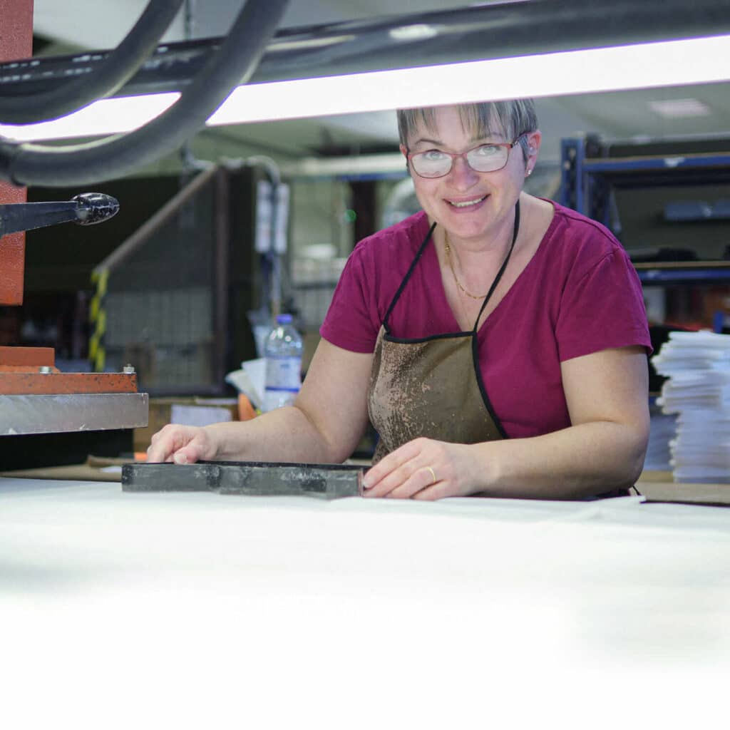 femme souriante, habillée en rose en train de travailler sur une machine dans un atelier