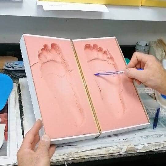empreintes de pieds dans une boite en mousse rose, une main et un stylo