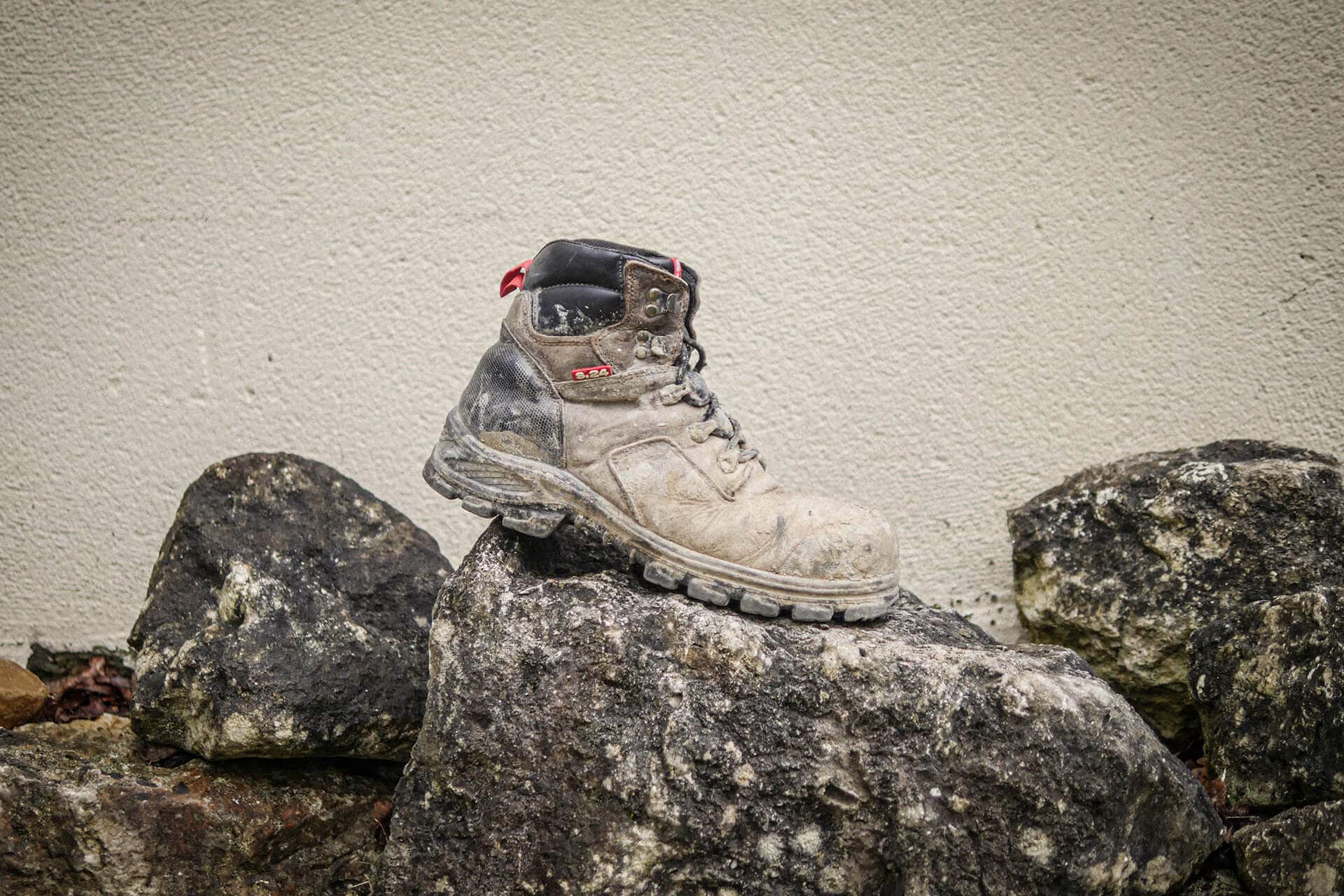 chaussure de sécurité sale posée sur une roche devant un mur