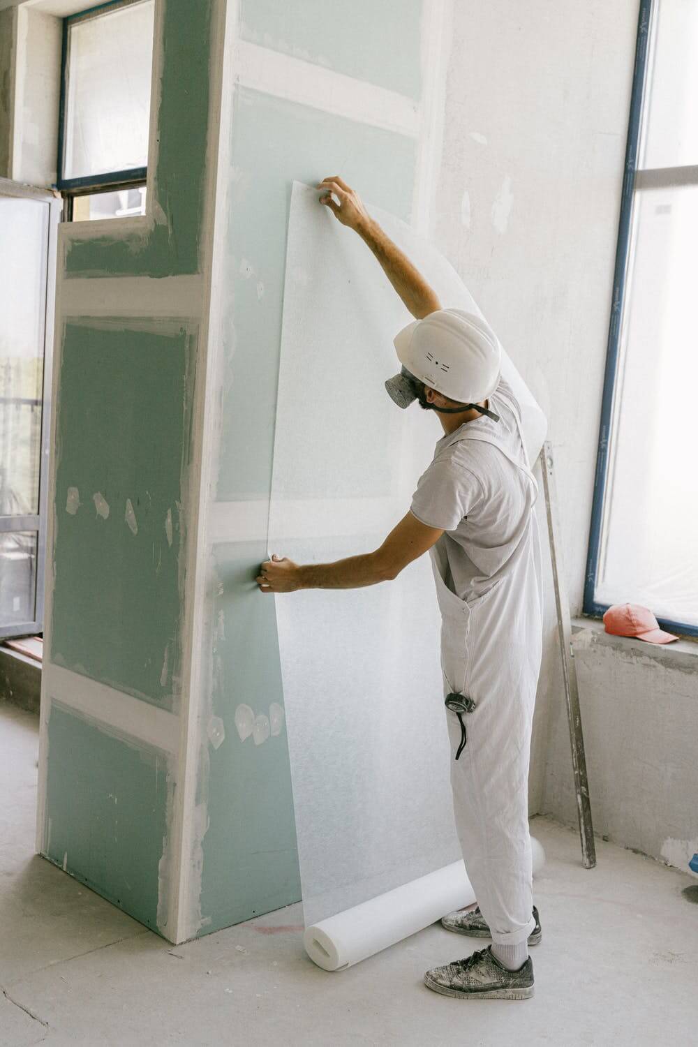 homme habillé en blanc avec un casque qui tend une toile sur un mur vert