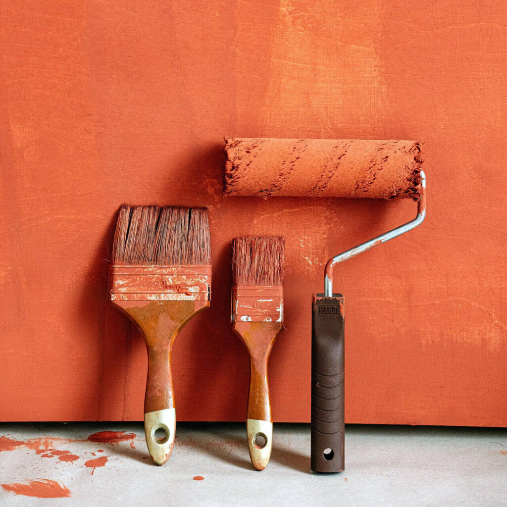 pinceaux et rouleau de peinture appuyés sur un mur orange