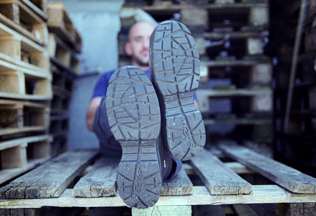 dessous des semelles de chaussures d'un homme assis sur une palette en bois