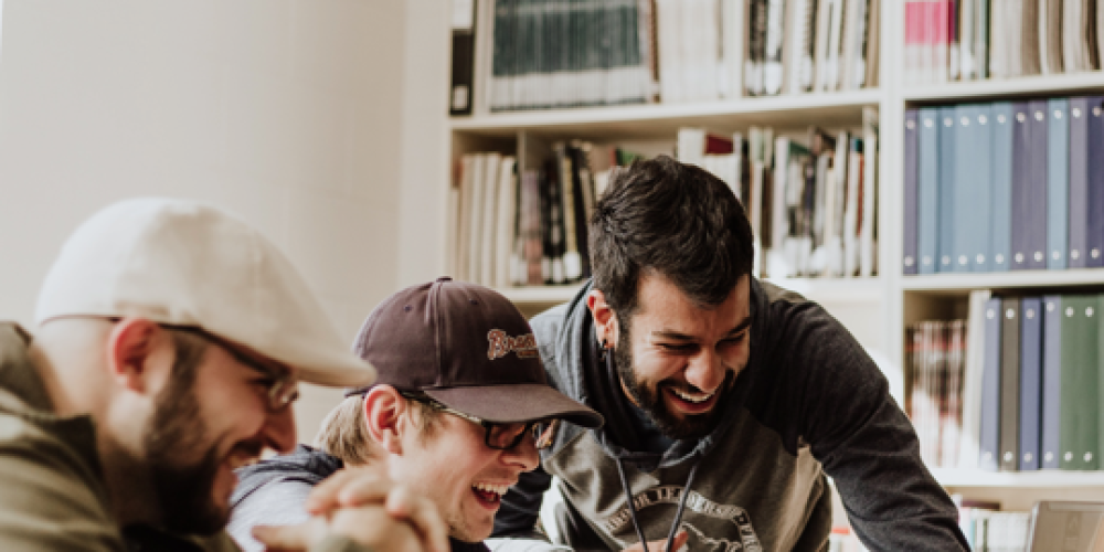 trois hommes qui rient devant un écran d'ordinateur