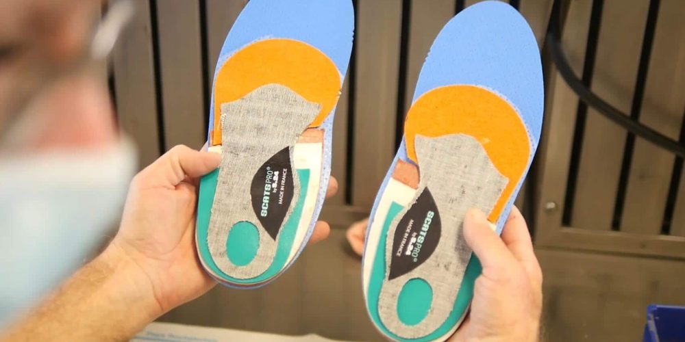 homme tenant une paire de semelles de confort multicolores