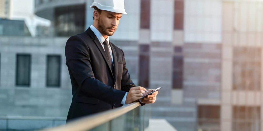homme en costume avec un casque en train de prendre des notes au milieu des building