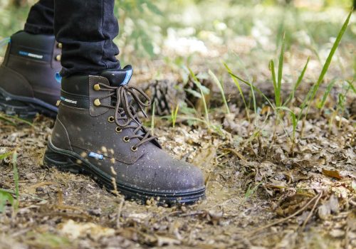 JUNGLE EVO ban 1920×1080 personne avec une chaussure de sécurité montante marron et noire qui marche dans une flaque d'eau en forêt