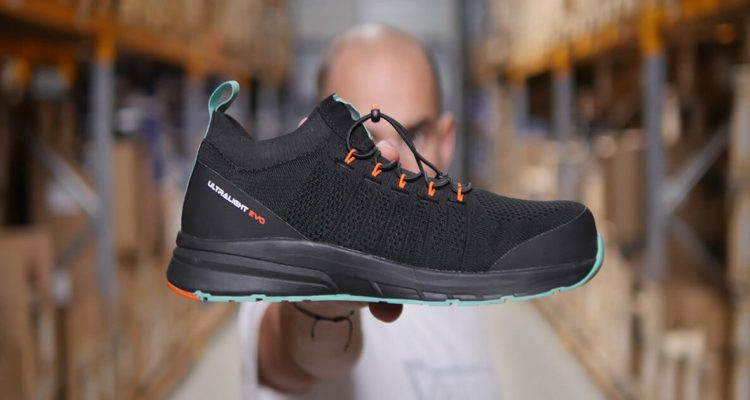 homme dans un entrepôt tenant une basket de sécurité noire, verte et orange