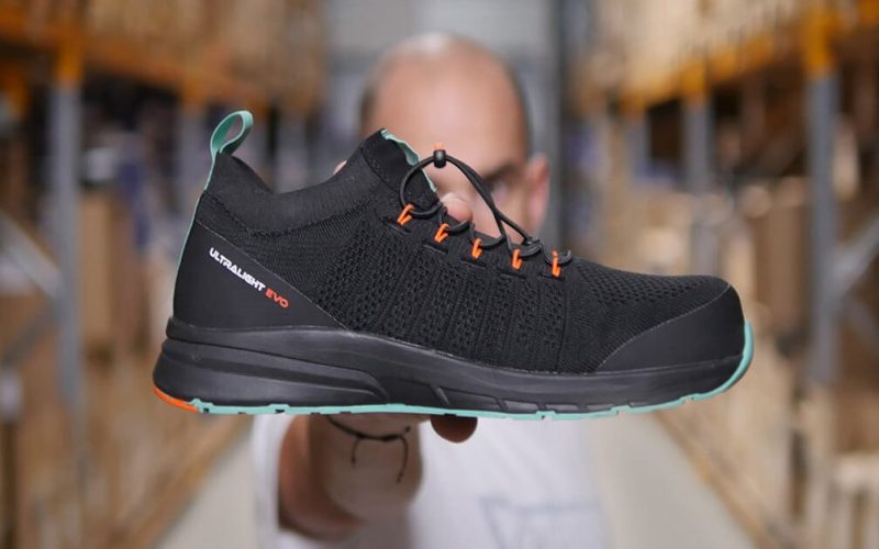 homme dans un entrepôt tenant une basket de sécurité noire, verte et orange