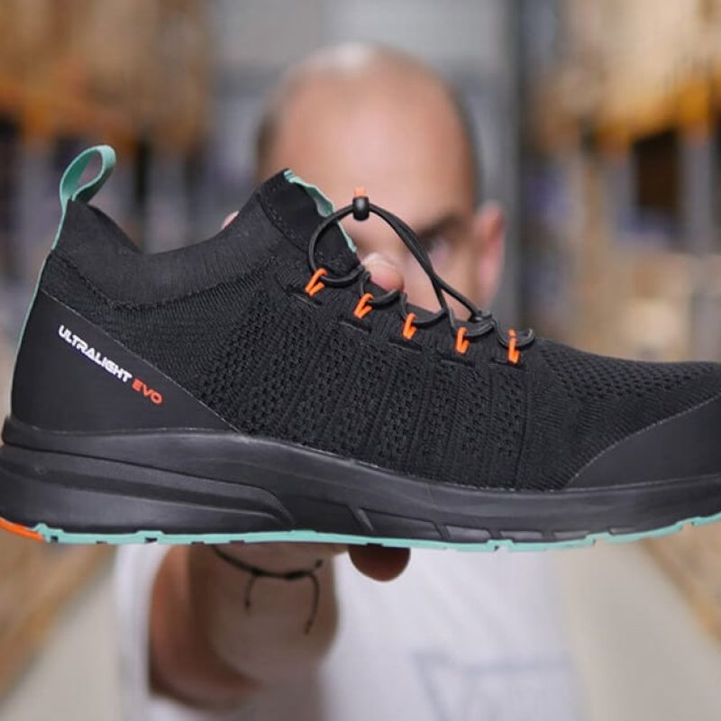 LUNAR 400 S1P chaussure de sécurité 1200×630 homme dans un entrepôt tenant une basket de sécurité noire, verte et orange
