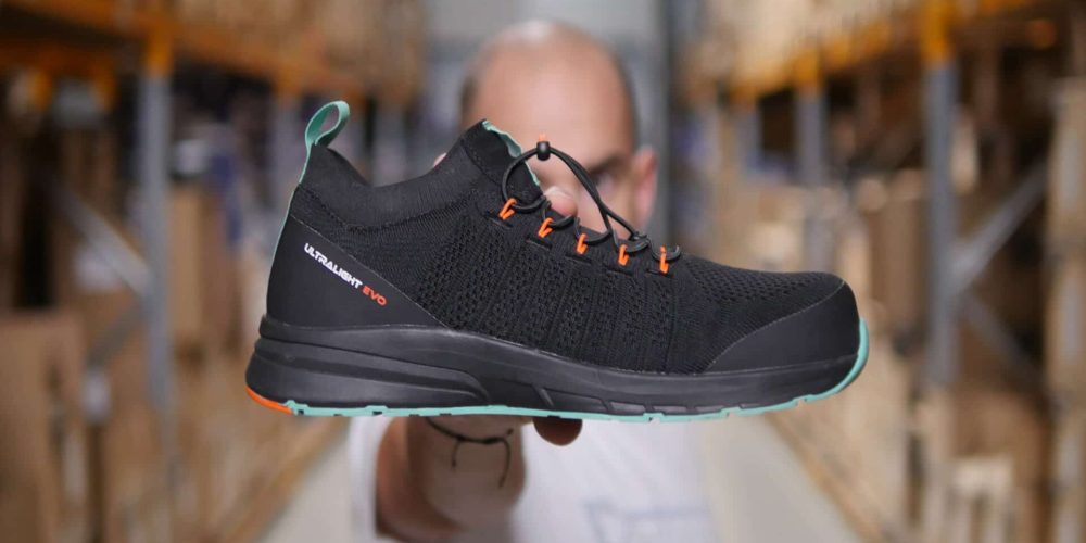 homme dans un entrepôt tenant une basket de sécurité noire, verte et orange