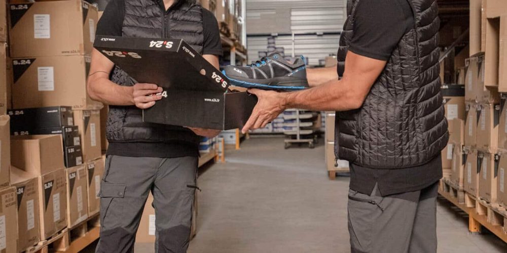 deux hommes debout dans un entrepôt en train de se donner une chaussure