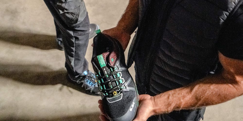 homme habillé en noir tenant une chaussure dans les mains