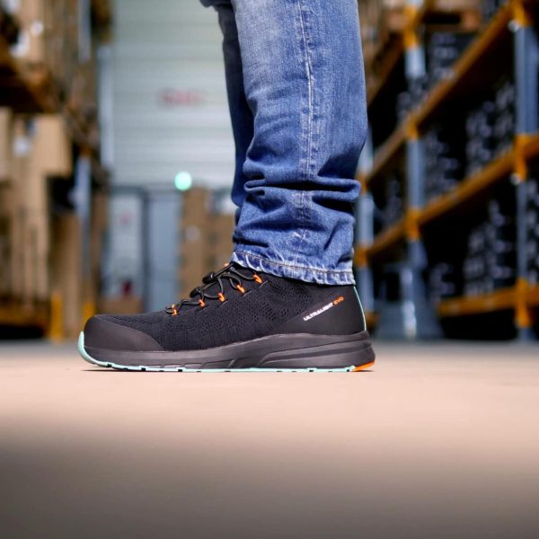 personne de profil dans un entrepôt habillée en jeans et avec des baskets de sécurité noires