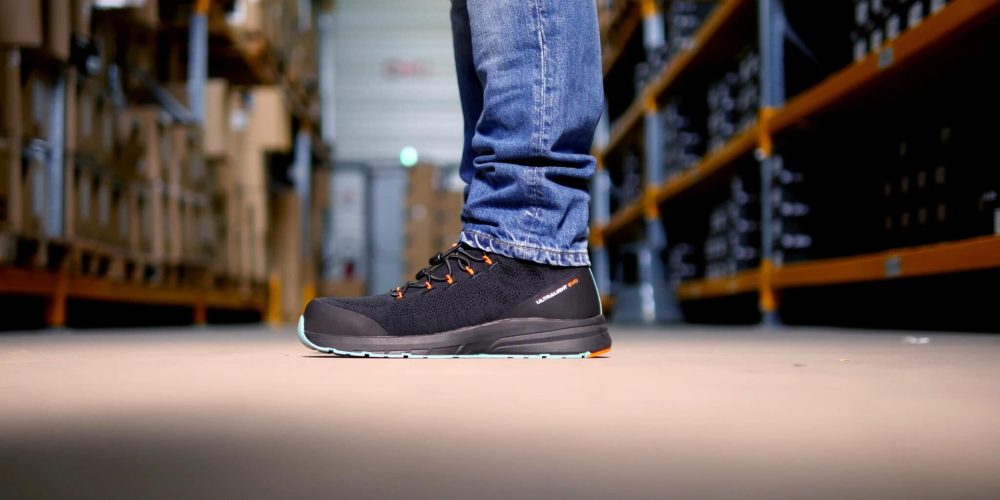 personne de profil dans un entrepôt habillée en jeans et avec des baskets de sécurité noires