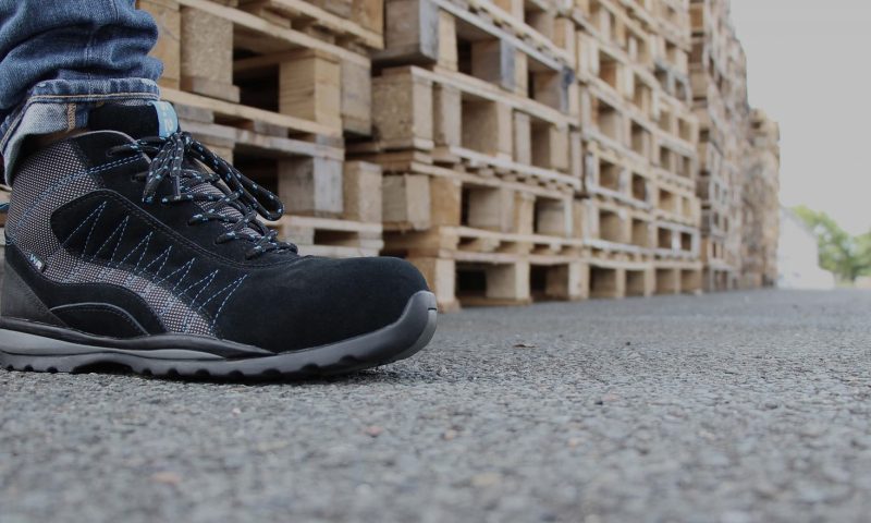 chaussure de sécurité montante noire et grise prise de profil devant des palettes en bois