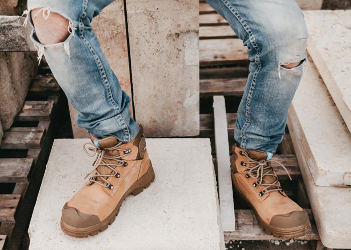 homme assis sur des blocs de pierre habillé avec un jeans et des chaussures de sécurité couleur crème