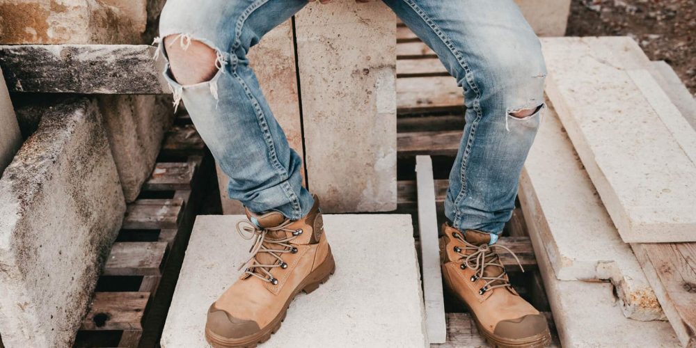 jambes d'une personne habillée un jeans troué et portant des chaussures de sécurité montantes marron