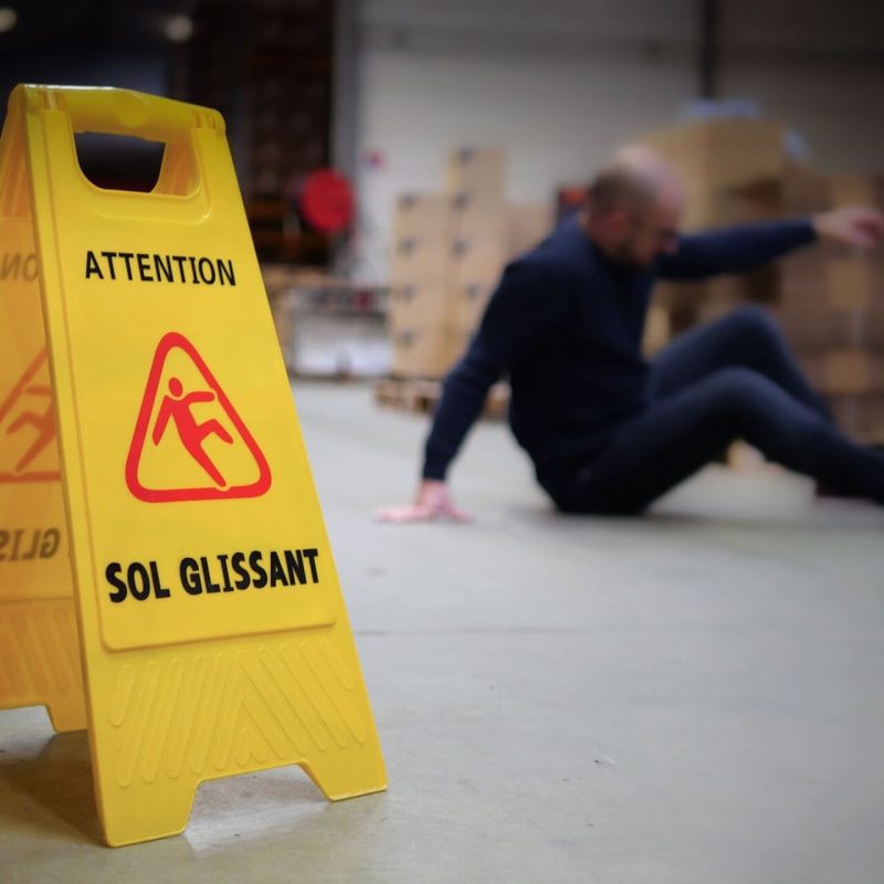 homme chute de plain-pied avec panneau signalétique jaune sol glissant
