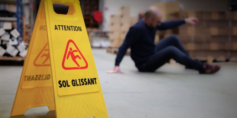 homme chute de plain-pied avec panneau signalétique jaune sol glissant