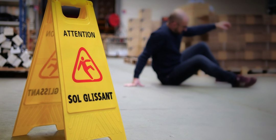 homme chute de plain-pied avec panneau signalétique jaune sol glissant