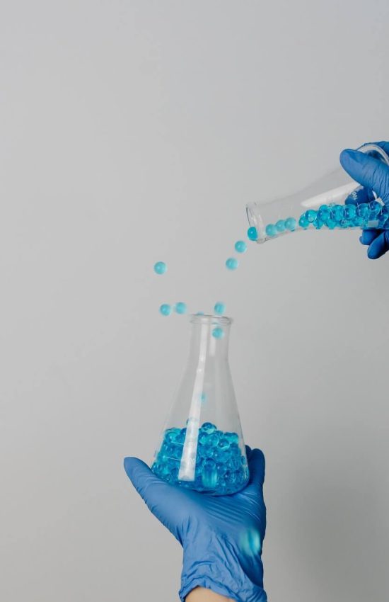 personne avec des gants bleus et des éprouvettes dans les mains remplies de billes bleues