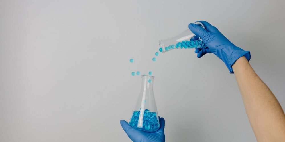 personne avec des gants bleus et des éprouvettes dans les mains remplies de billes bleues