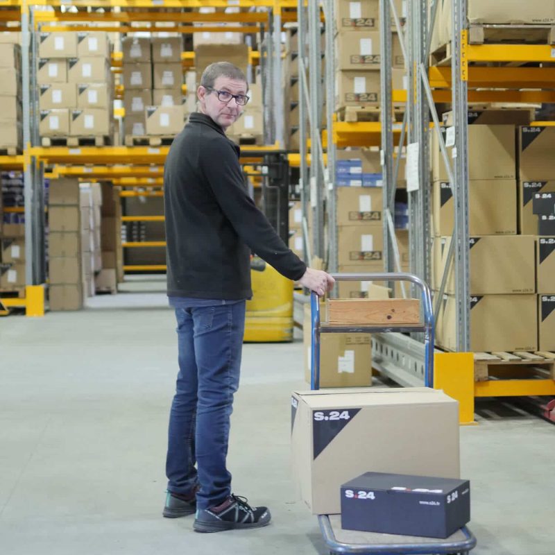 homme debout dans un entrepôt tirant un charriot