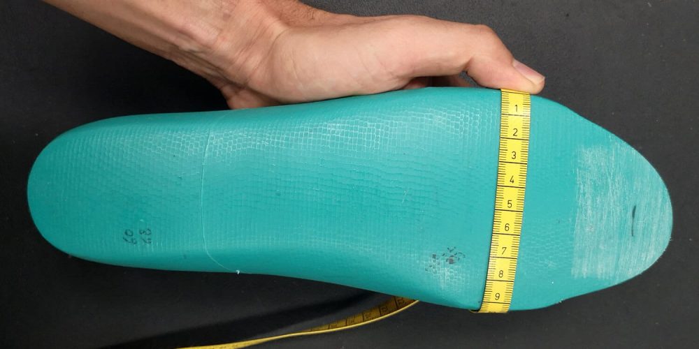 main tenant une forme en plastique verte avec un mètre ruban