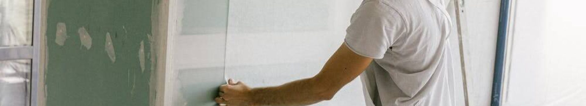 peintre batiment homme habillé en blanc avec un casque qui tend une toile sur un mur vert