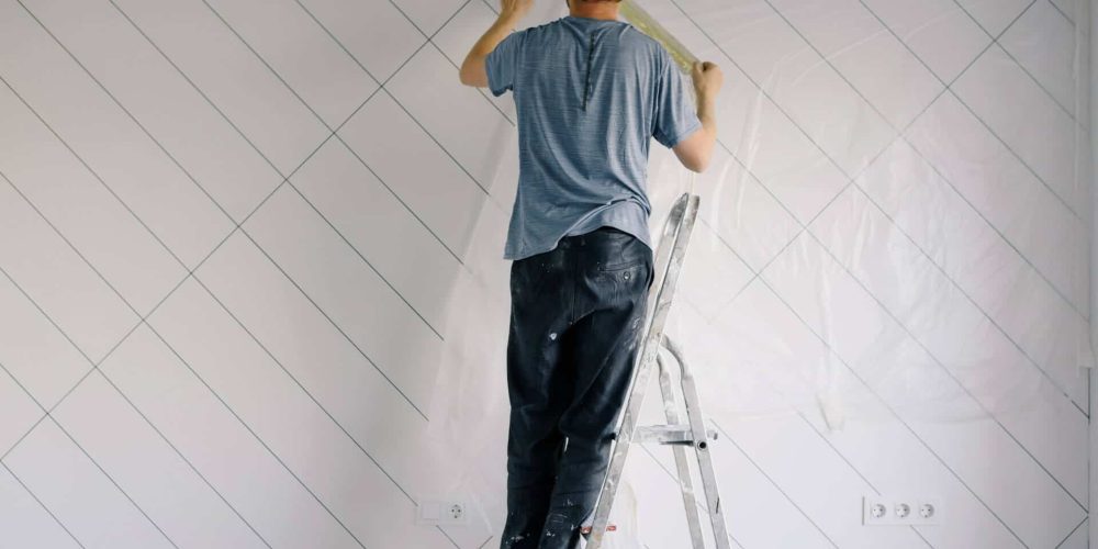 homme de dos sur un escabeau en train de tracer des repères sur un mur