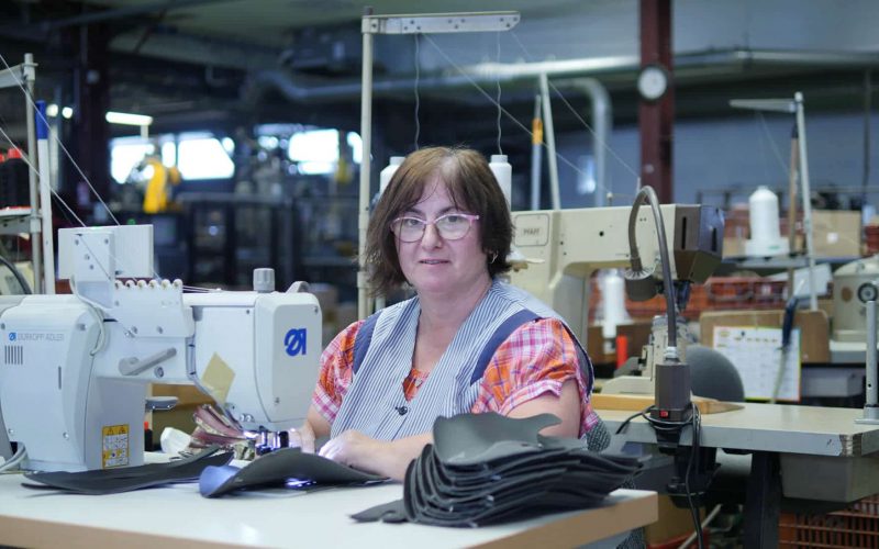femme avec des lunettes et un tablier qui travaille sur une machine à coudre dans un atelier