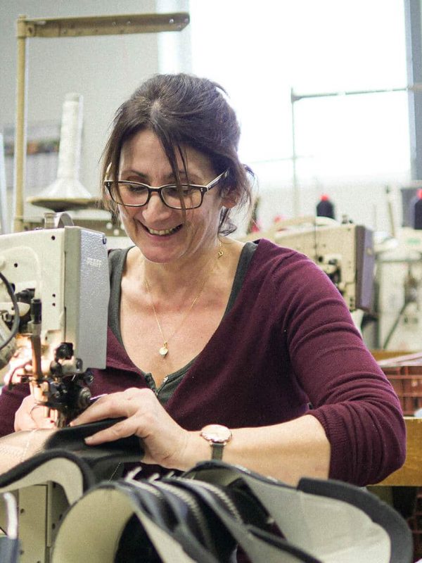 femme avec des lunettes souriante qui travaille sur une machine à coudre dans un atelier