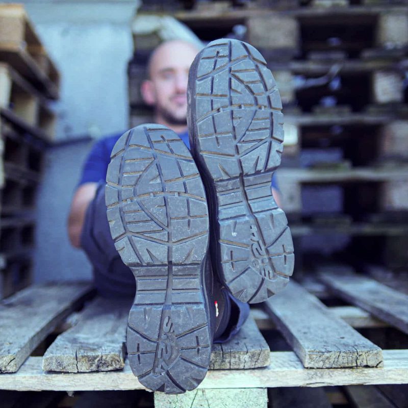 dessous des semelles de chaussures d'un homme assis sur une palette en bois