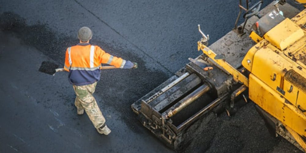 machine et homme en orange sur de l'enrobé